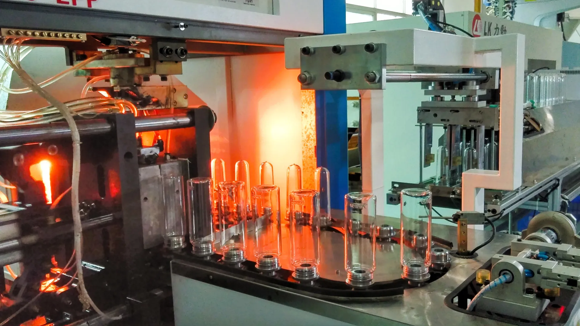 An automated blow-moulding line in production, clear bottles turning on the carousel past the glowing heaters before moving off along the conveyor